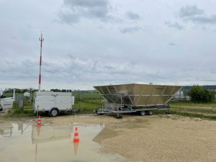 Figure 1 : Le profileur de vent mobile installé à Granges à côté de la station SwissMetNet (réseau automatique de mesures au sol). La petite remorque à gauche abrite l'électronique pour la saisie et la transmission des données de mesure. A droite, derrière le radar mobile, on peut voir le radar fixe Windprofiler qui doit être remplacé.