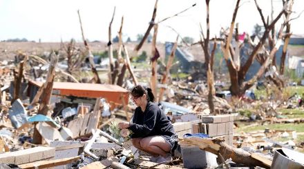 Figure 5 : Kimberly Ergish porte des fleurs et reste pensive lors de la récupération de restes de ses affaires parmis les débris laissé derrière suite au passage d’une tornade sur son habitation le 22 mai 2024 à Greenfield dans l’Iowa.