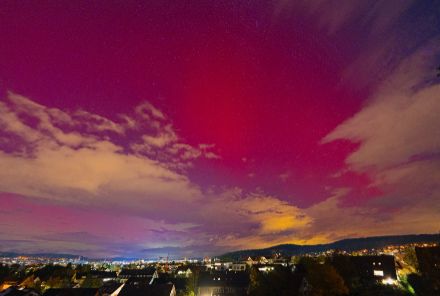 Aurore boréale rouge dans le ciel nocturne au-dessus des lumières de la ville de Winterthur.