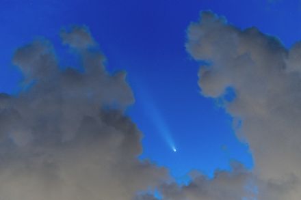 Comète dans le ciel bleu du soir entre des nuages gris.