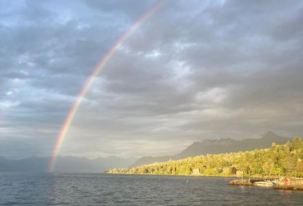 Arc-en-ciel en bord de lac, sur fond de ciel nuageux, côte au soleil