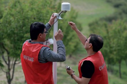 Deux hommes installent un capteur météo en plein air.