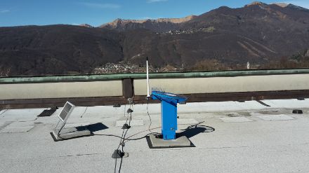 Un capteur de grêle en métal bleu surmonté d’un écran en polycarbonate. À gauche du capteur, un panneau solaire.