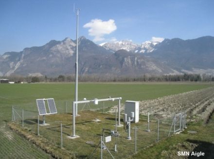 Image d'une station météorologique clôturée avec des appareils de mesure sur une prairie verte. 