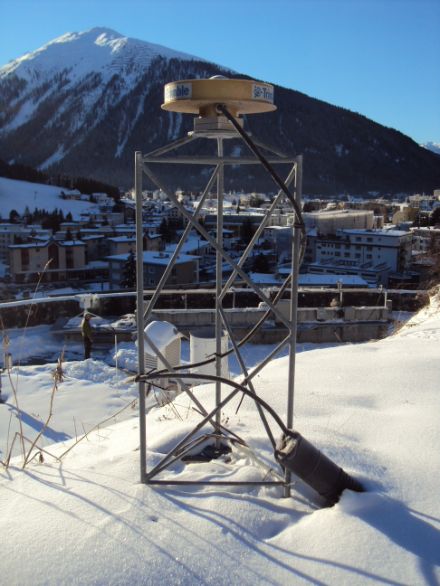 Situé au premier plan de l'image, l'appareil topographique GPS est formé d'un disque monté sur un châssis métallique. Il est possible de reconnaître Davos à l'arrière-plan.