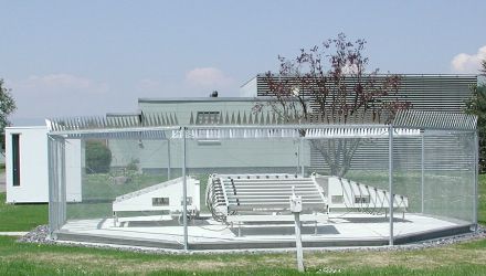 Au centre de la photo, antennes en forme de tuyaux blancs parallèles, entourées d'une barrière métallique de deux mètres de haut.