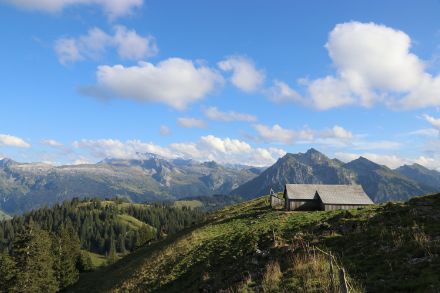 Un chalet d'alpage en montagne, surmonté d'un ciel d'un bleu profond avec quelques cumulus.