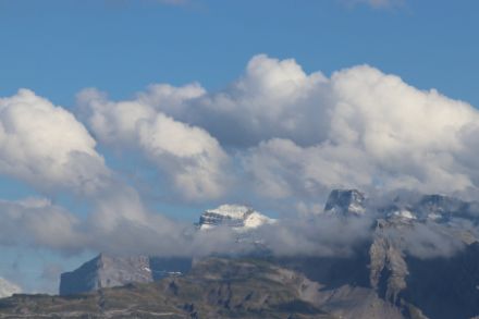 Vue sur une montagne enneigée entourée de cumulus. Au-dessus, un ciel bleu.