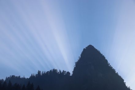 Rayons crépusculaires apparaissant en éventail derrière une montagne et rayonnant vers le haut.
