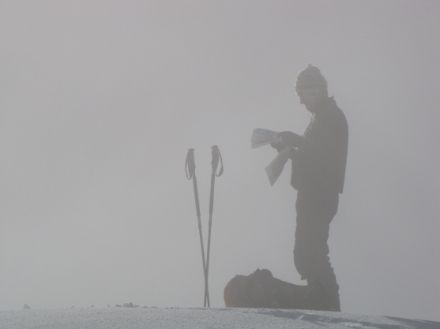 Image d'un skieur de randonnée dans le brouillard, consultant une carte.