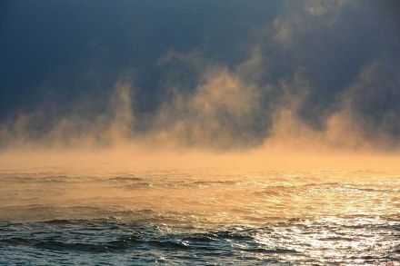 Brouillard d’évaporation sur un lac illuminé en orange par lumière du soleil.