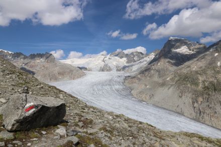 Photo du glacier du Rhône par temps légèrement nuageux. Au premier plan, on peut voir un panneau de randonnée.