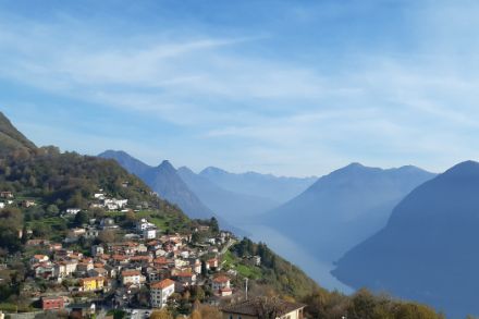 Petit village de montagne avec des montagnes et un lac en arrière-plan. Ciel bleu avec voiles nuageux. 