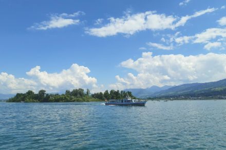 Île boisée au milieu d'un lac, ciel bleu avec des nuages, bateau devant l'île.