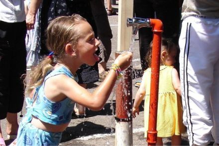 Une fillette étanche sa soif auprès d'un robinet d'eau.